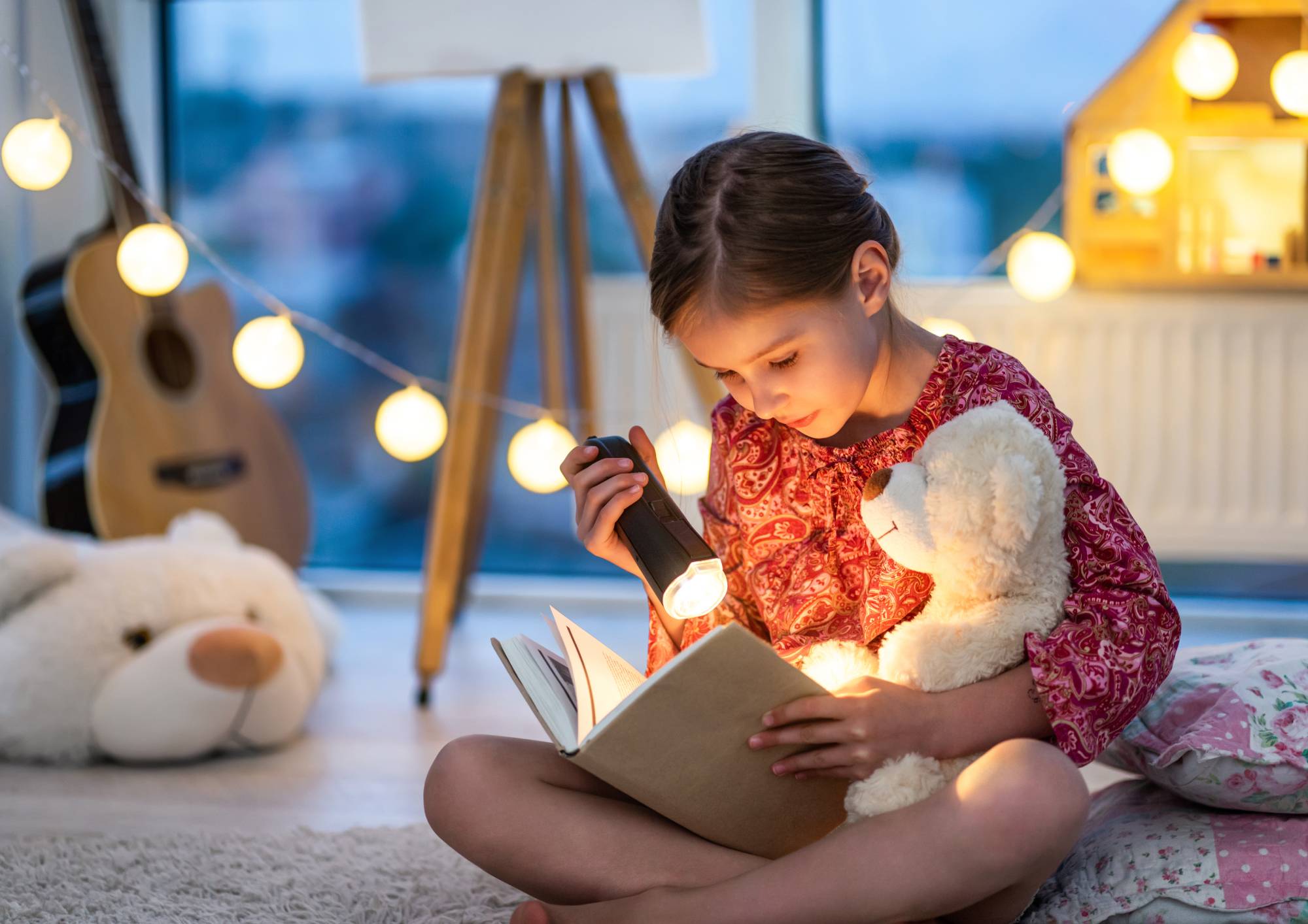 Kind liest ein Buch bei eingeschalteter Tischleuchte im Zimmer