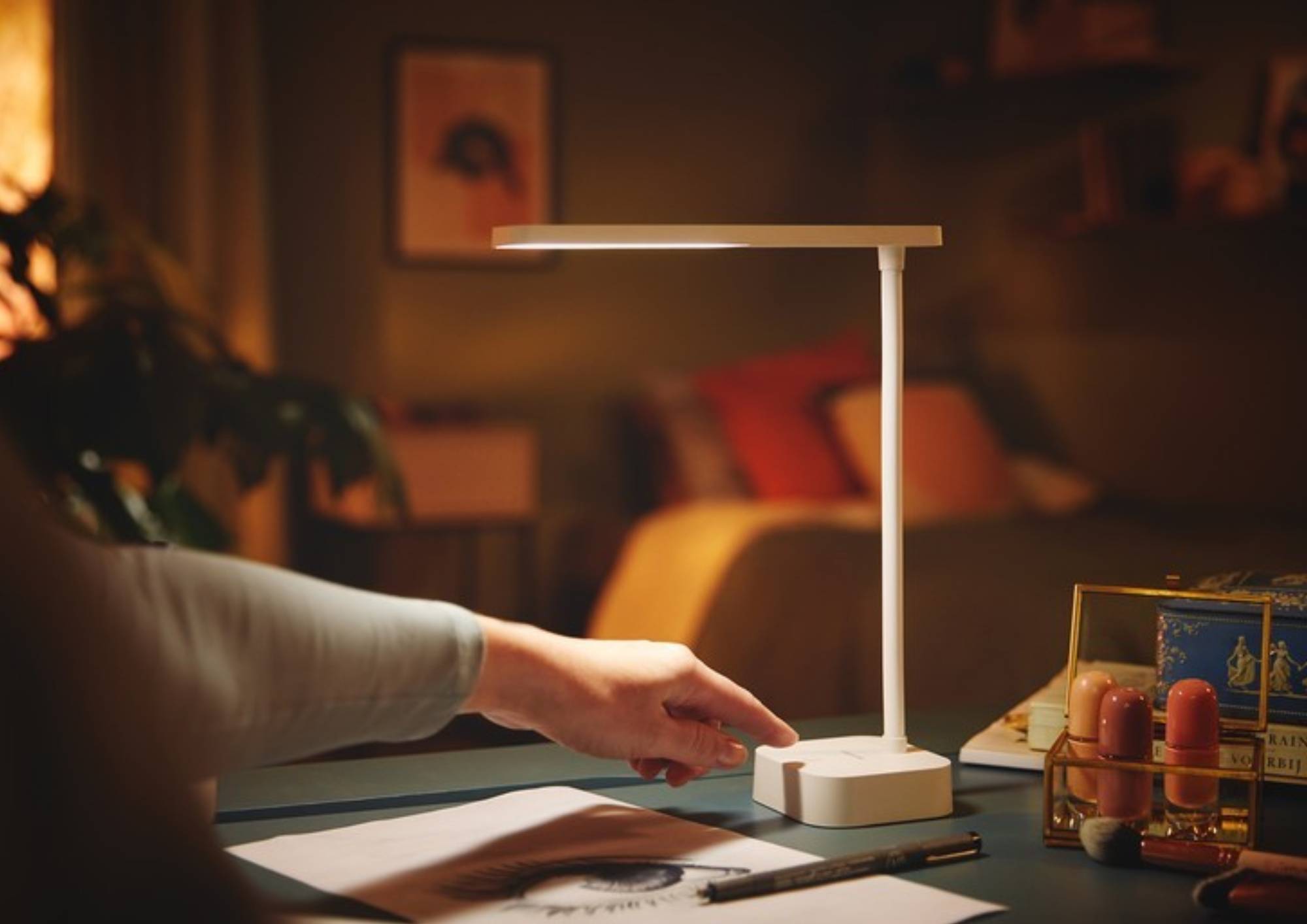 Hand schaltet eine Schreibtischleuchte auf dem Tisch ein