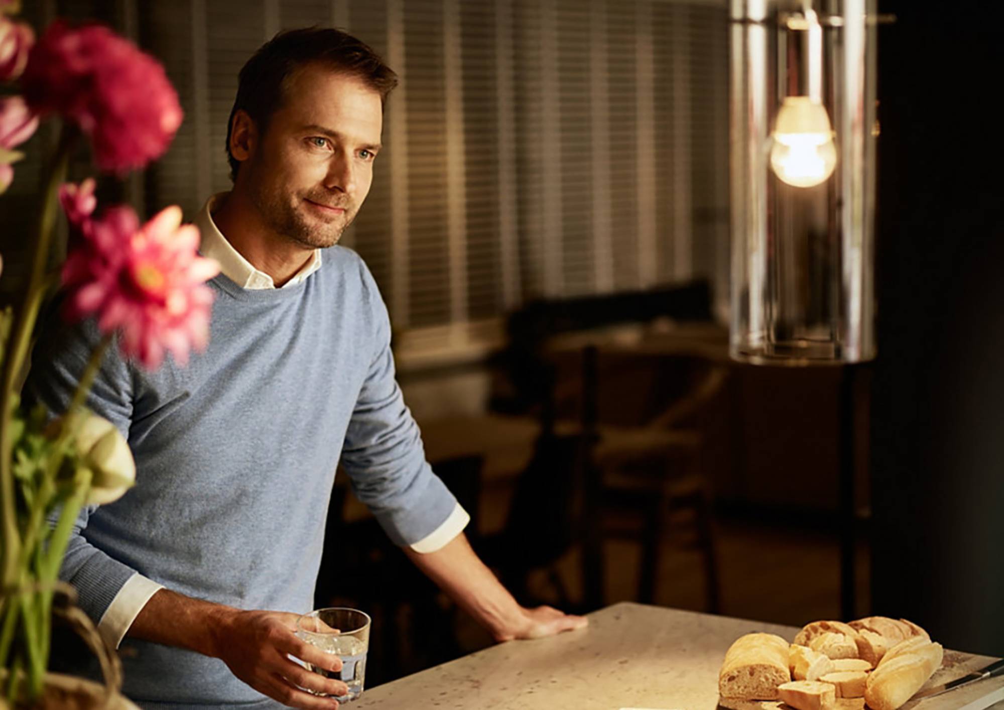 Mann steht an der Küchenarbeitsplatte bei eingeschalteter Pendelleuchte