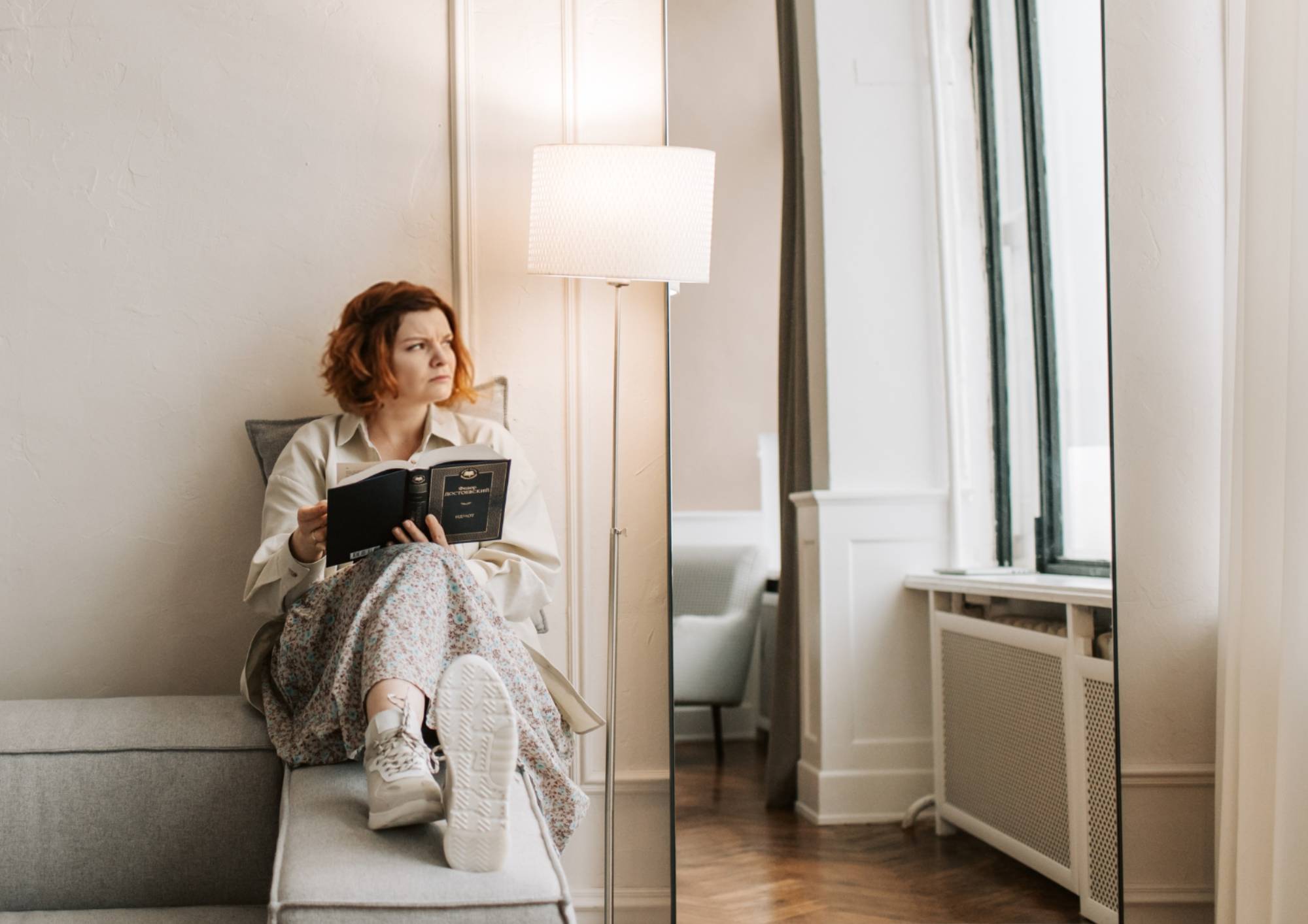 Frau sitzt auf dem Sofa bei eingeschalteter Stehleuchte im Wohnzimmer