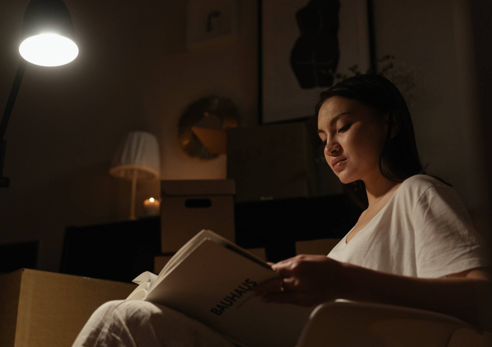 Frau liest ein Buch bei eingeschalteter Leuchte in gedimmtem Innenraum